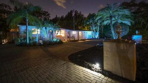 A well-lit building with a paved entrance, palm trees, and a flagpole.