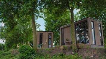 A modern cabin with large windows and a wooden exterior, surrounded by lush greenery and trees.