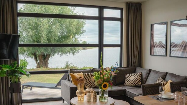 Ein modernes Wohnzimmer mit großem Fenster mit Seeblick, einer Couch, einem Couchtisch und einem Essbereich.