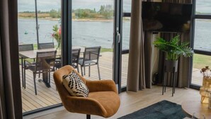 Ein modernes Wohnzimmer mit großem Fenster mit Seeblick, einem bequemen Sessel, einem Essbereich und einem Flachbildfernseher.