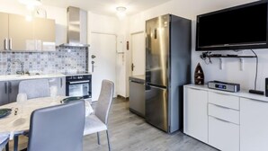 Eine moderne Küche mit einem Edelstahl-Kühlschrank, einem Esstisch mit Stühlen, einem an der Wand montierten Fernseher und einer gemusterten Spritzschutzwand.
