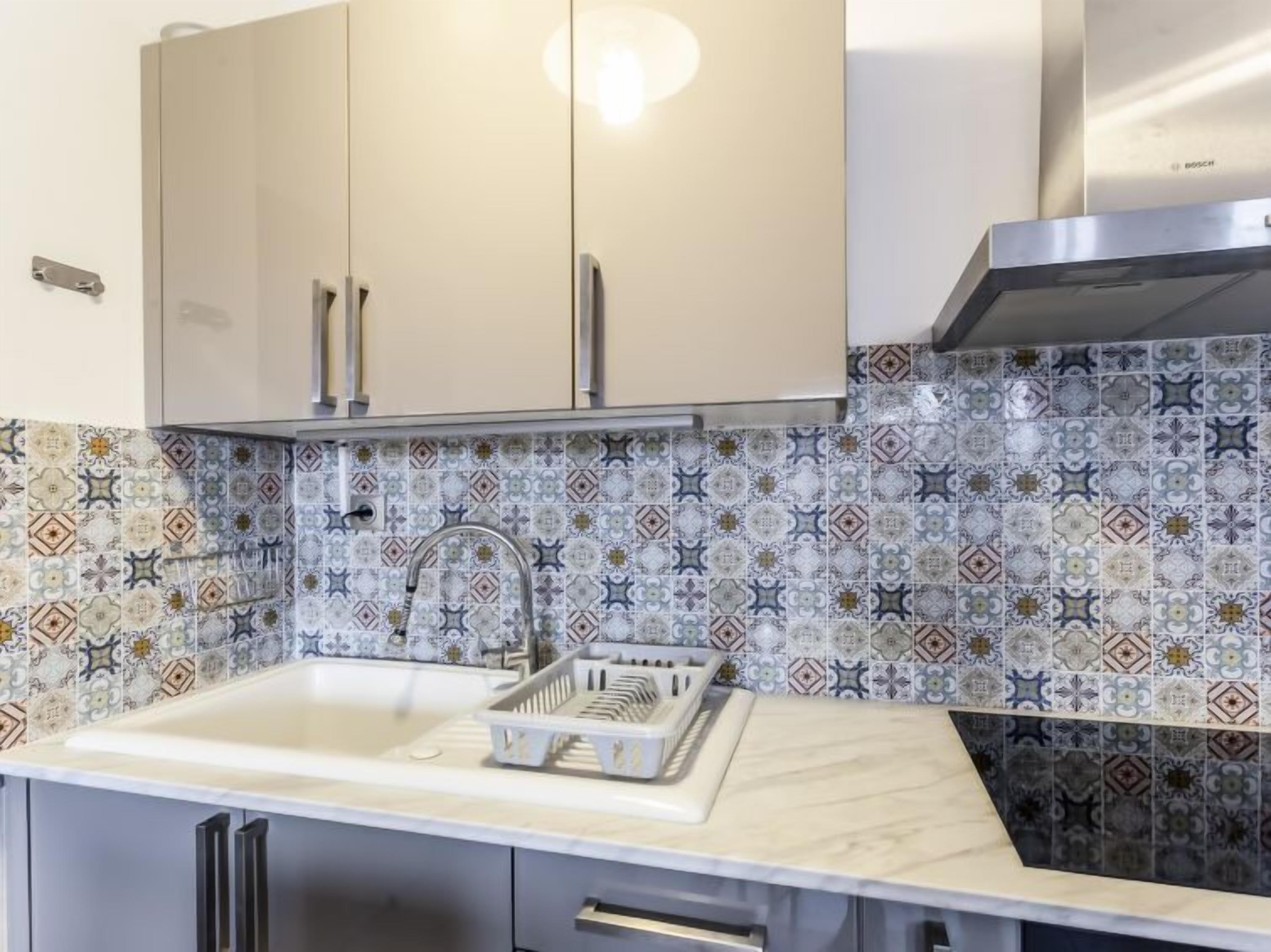 A kitchen with a white sink, patterned backsplash, and stainless steel cabinets.