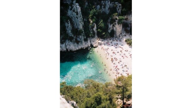 Ein Strand mit klarem türkisblauem Wasser, umgeben von felsigen Klippen und dichter Vegetation.