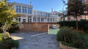 A courtyard with a brick wall, a green gate, and a row of white buildings with multiple windows. - Serendipity Apartment-Your home in Venice (Venezia)