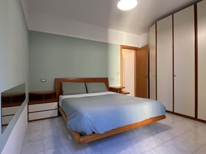 Une chambre à coucher avec un lit, une tête de lit en bois, des tables de chevet, une armoire et un interrupteur sur le mur.