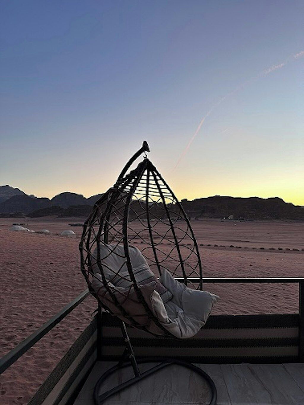 A beach view with a hanging chair and a wooden deck.