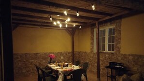 Un coin repas avec une table ronde dressée pour quatre personnes, entourée de chaises. La pièce est dotée d’un mur en pierre rustique et d’un plafond en bois.