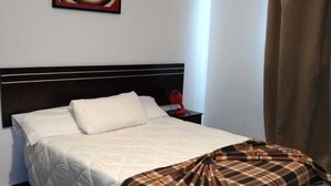 Un lit bien fait, avec une couverture à carreaux, une tête de lit et un tableau accroché au mur.