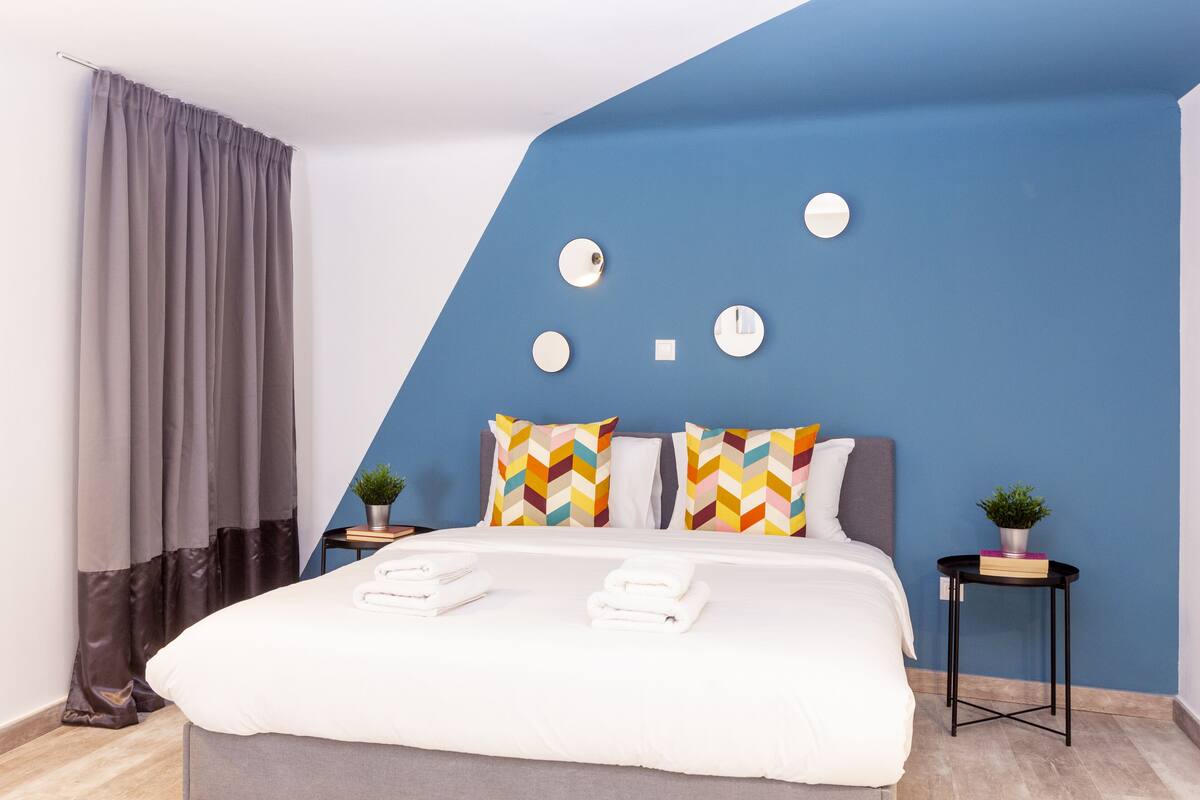 A modern bedroom with a large bed, grey curtains, a blue accent wall, and decorative circular elements.