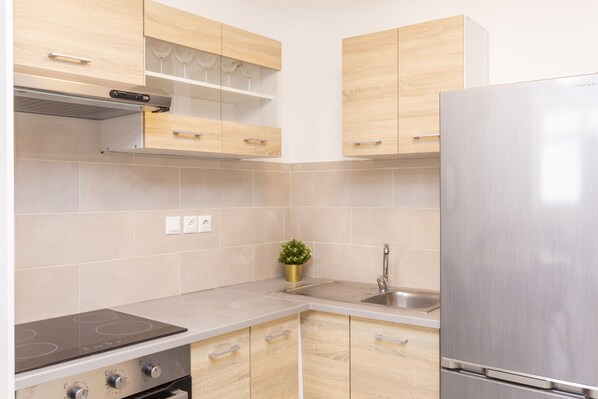 A modern kitchen with light wood cabinets, a stainless steel refrigerator, a built-in oven, and a small potted plant.