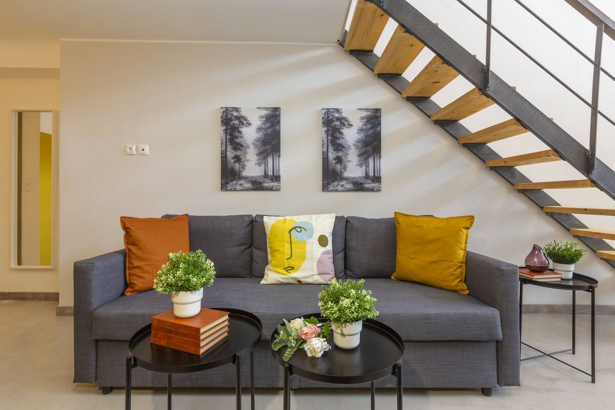 A modern living room with a grey sofa, two black coffee tables, and a staircase with wooden steps.