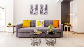 Un salon moderne avec un canapé gris, deux tables rondes à structure métallique et une petite table d’appoint blanche agrémentée d’une plante.