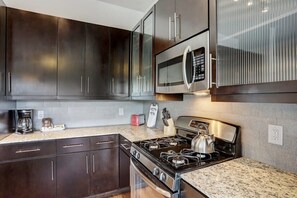 Cozinha moderna com armários escuros, micro-ondas de aço inoxidável, fogão a gás e bancada de granito.