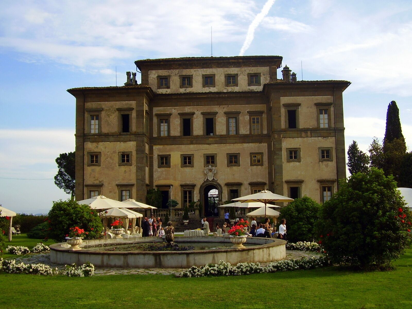 Un edificio storico imponente con un cortile centrale, circondato da vegetazione lussureggiante e una fontana.
