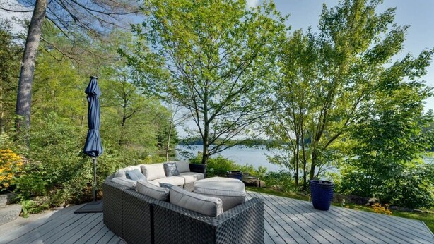 A deck with a wicker sofa, a blue umbrella, and a view of a lake.