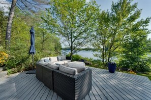 Una terraza con un sofá de mimbre, un paraguas azul y vista a un lago.