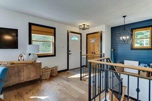 A modern interior with a wooden floor, a blue accent wall, a staircase with black railings, and a flat-screen TV mounted on the wall. - La Belle Vue - Beautiful Sunsets on Long Lake (Torrance)