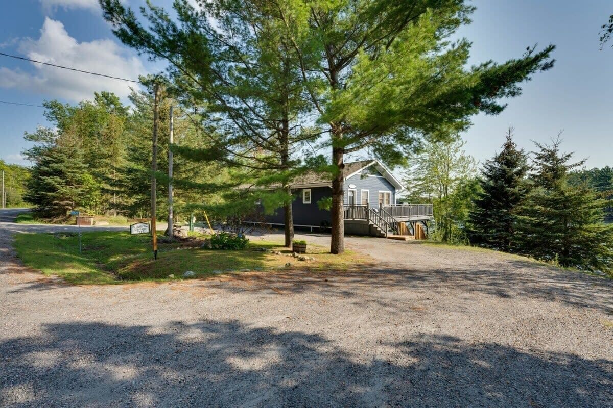 A house with a gravel driveway, surrounded by trees and a clear sky.