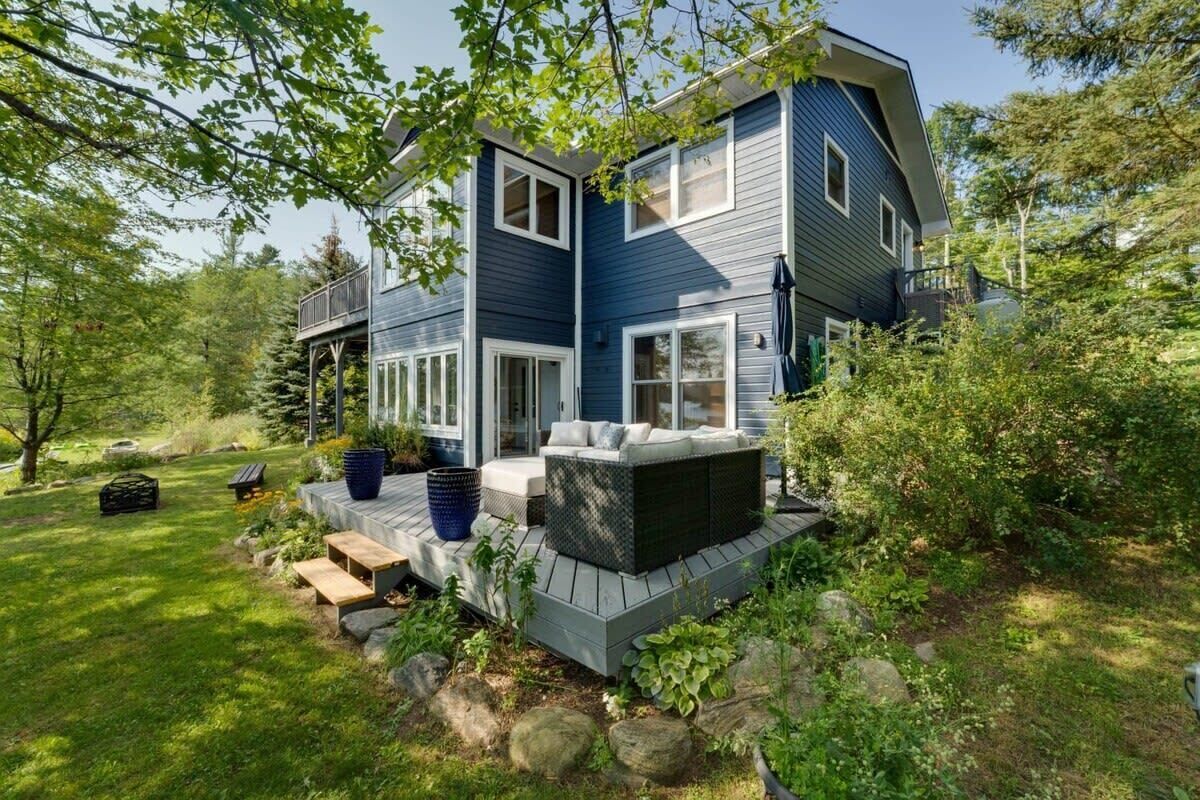 A two-story house with a deck, surrounded by a well-maintained garden and trees.