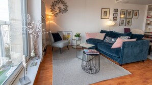 A modern living room with a blue sofa, a small round coffee table, and a large window providing a view of the outdoors. - MONTMARTRE, PARIS VIEW, ATTRACTIONS, 30–60 days ahead? Ask Private offer VIE-VAp (Paris)