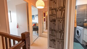 A hallway with a wooden railing, a glass partition with books, a washing machine, and a hanging light fixture. - MONTMARTRE, PARIS VIEW, ATTRACTIONS, 30–60 days ahead? Ask Private offer VIE-VAp (Paris)