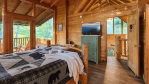 Ein Schlafzimmer in einer Holzhütte mit einem Bett, einem Fernseher und Blick ins Freie.