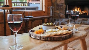 Ein Holztisch mit einer Wurstplatte, zwei Gläsern Rotwein und einem Kamin im Hintergrund.