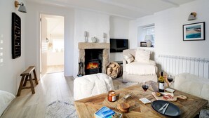 A cozy living room with a stone fireplace, a comfortable sofa, a coffee table with food and drinks, and a television on the wall. - This charming 18th Century cottage is centrally located in the heart of St Teath (St Teath)
