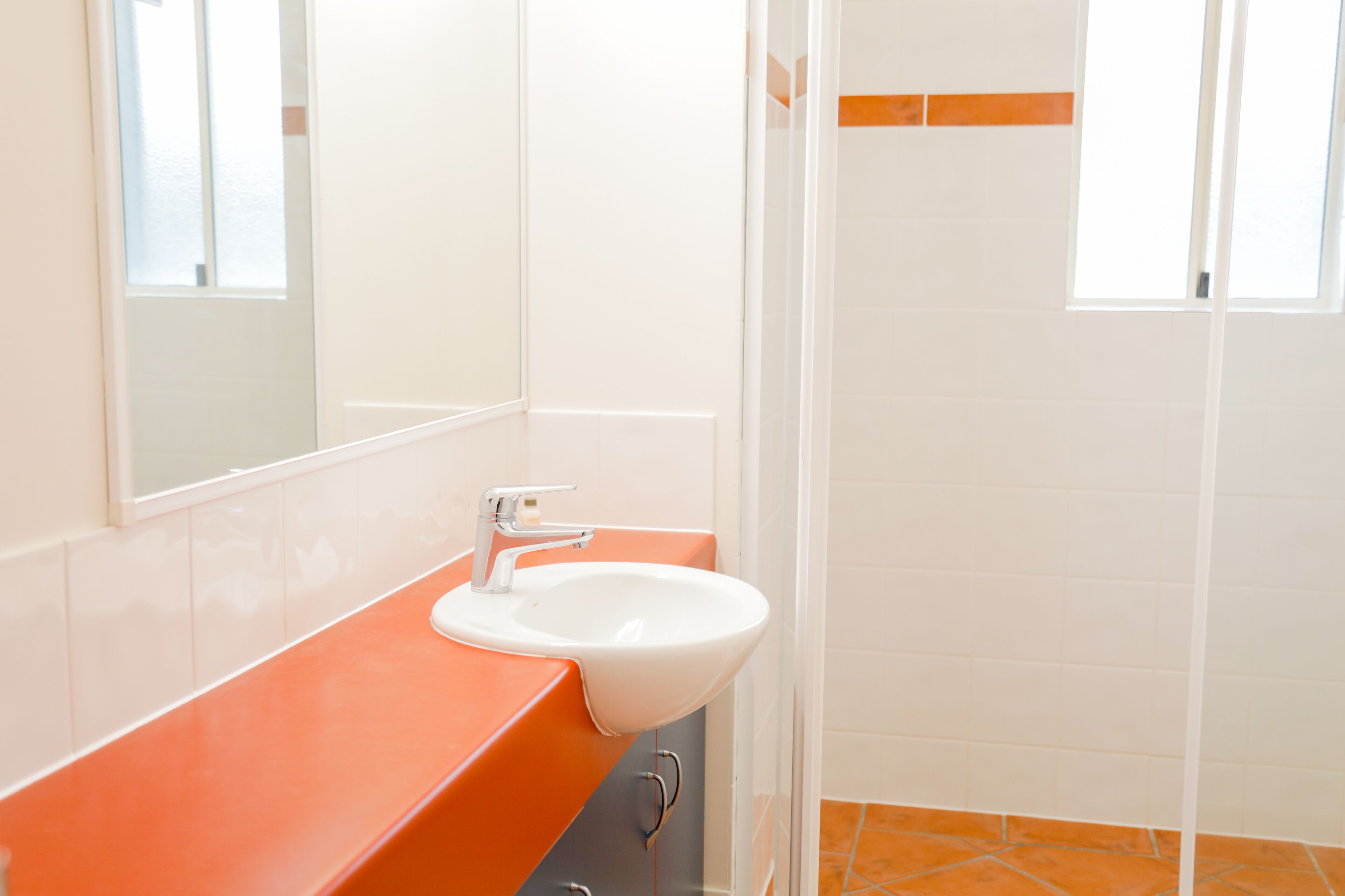 A bathroom with a white sink, orange countertop, and a mirror.