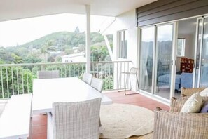 Un balcón con una mesa y sillas de comedor, un sofá y vistas a una ladera.