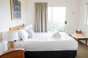 Habitación de hotel con una cama grande, una mesita de noche, una lámpara, una ventana con cortinas y un cuadro en la pared.
