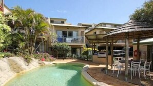 A swimming pool with a curved edge, surrounded by a patio area with outdoor seating. - Straddie Breeze - A gorgeous fully renovated beachside apartment (Point Lookout)