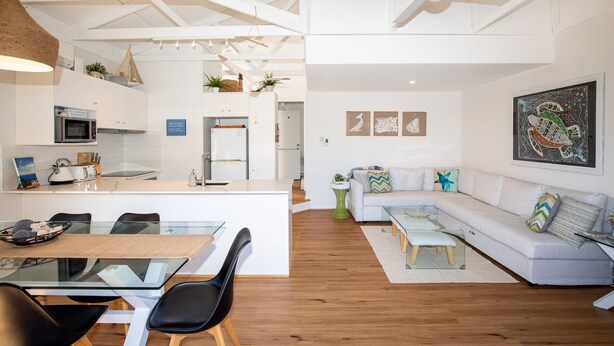 A modern living space with a kitchen, dining area, and a living room with a sofa and coffee table. - Straddie Breeze - A gorgeous fully renovated beachside apartment (Point Lookout)
