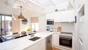 A modern kitchen with white cabinetry, a built-in microwave, a stove, and a dishwasher. - Straddie Breeze - A gorgeous fully renovated beachside apartment (Point Lookout)