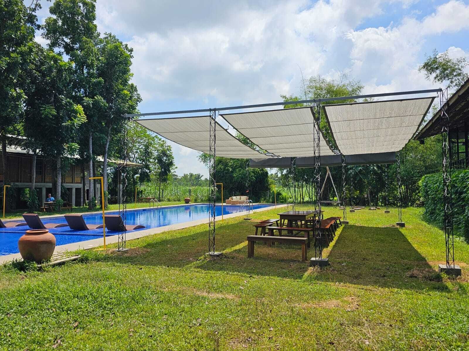 Zona de piscina con área de estar cubierta, sillas de descanso y una mesa de picnic.