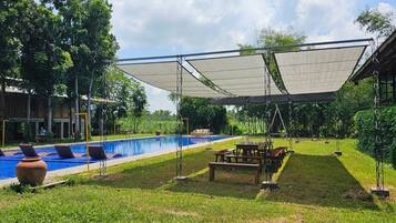 Zona de piscina con área de estar cubierta, sillas de descanso y una mesa de picnic.