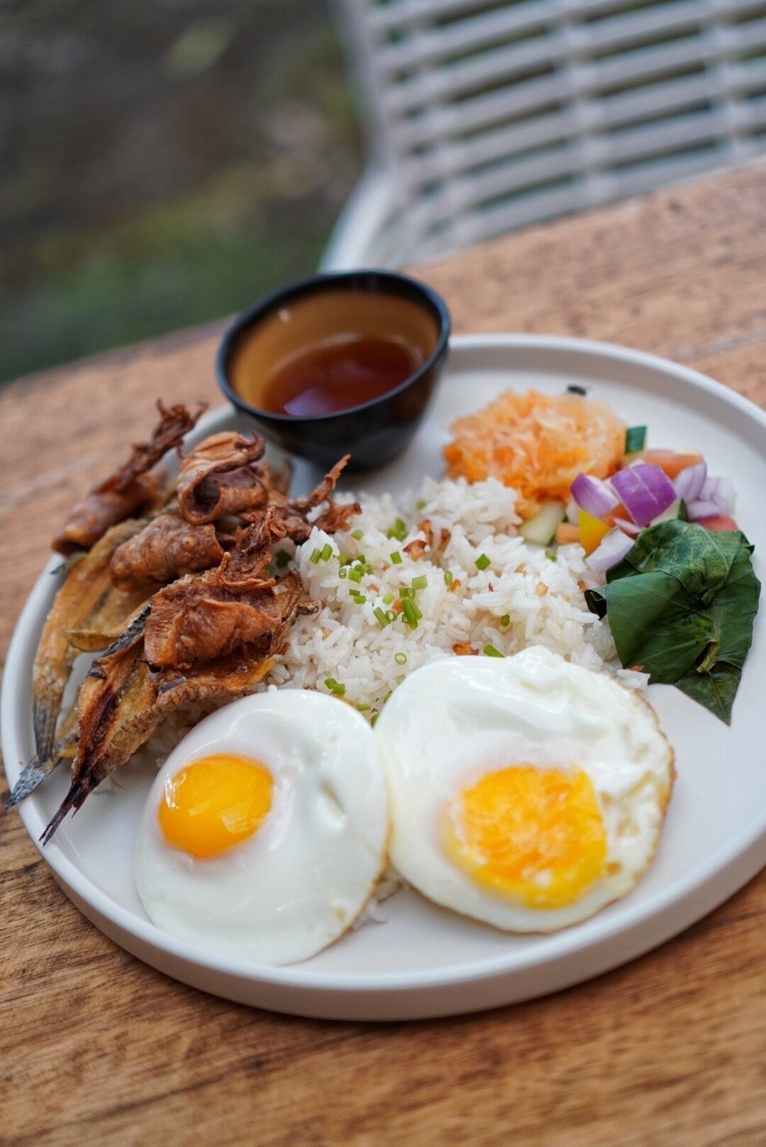Une assiette de poisson frit, de riz et d’œufs, accompagnée d’un accompagnement de légumes et d’un petit bol de sauce.