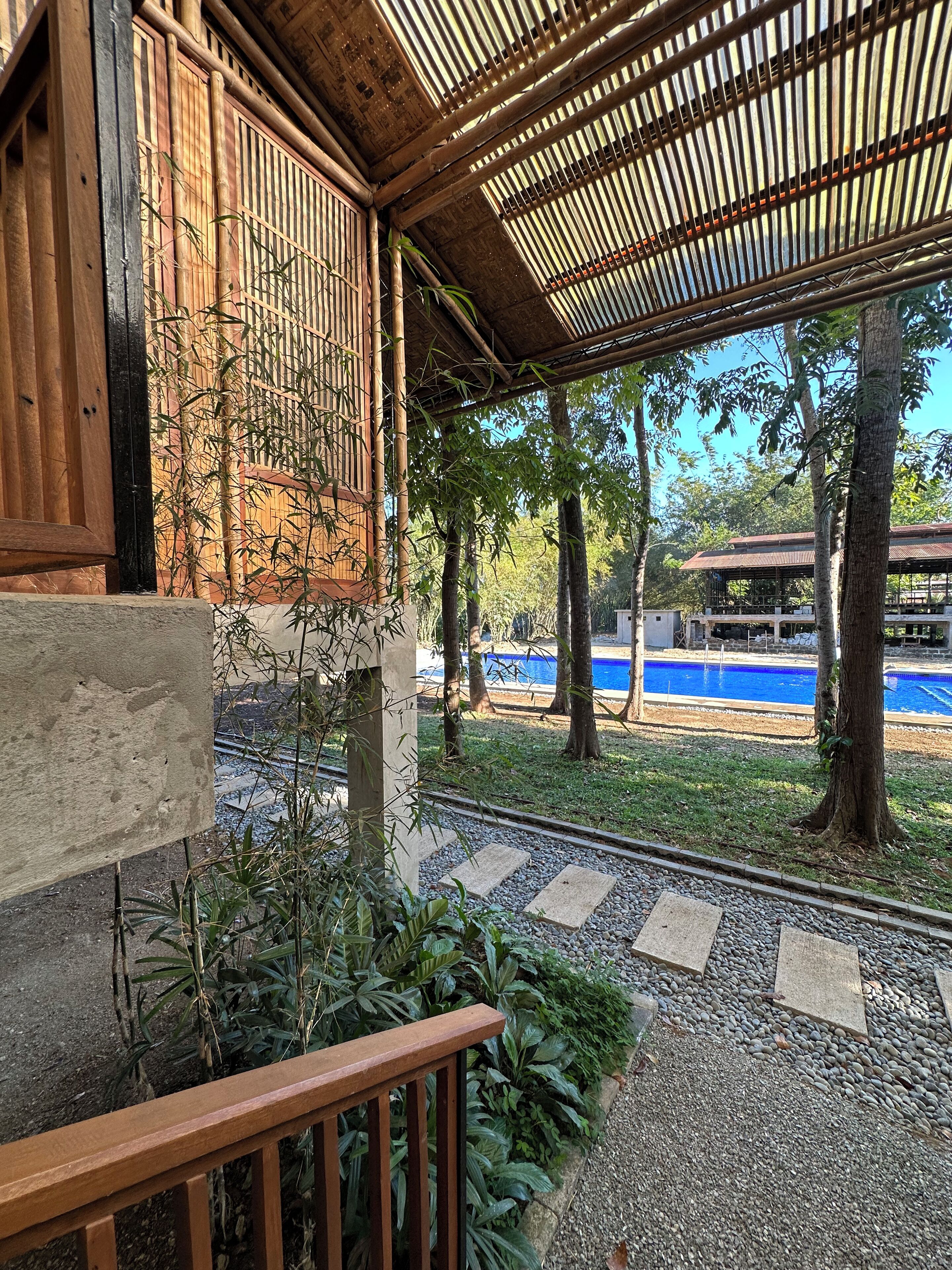 A covered outdoor area with a wooden structure, a pool, and a garden with trees and plants.