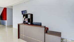 A modern reception desk with a flat-screen TV, a vase of flowers, and a small table with a decorative item. - Hotel O Beda Arga Near Rs Royal Prima Ayahanda (Medan)