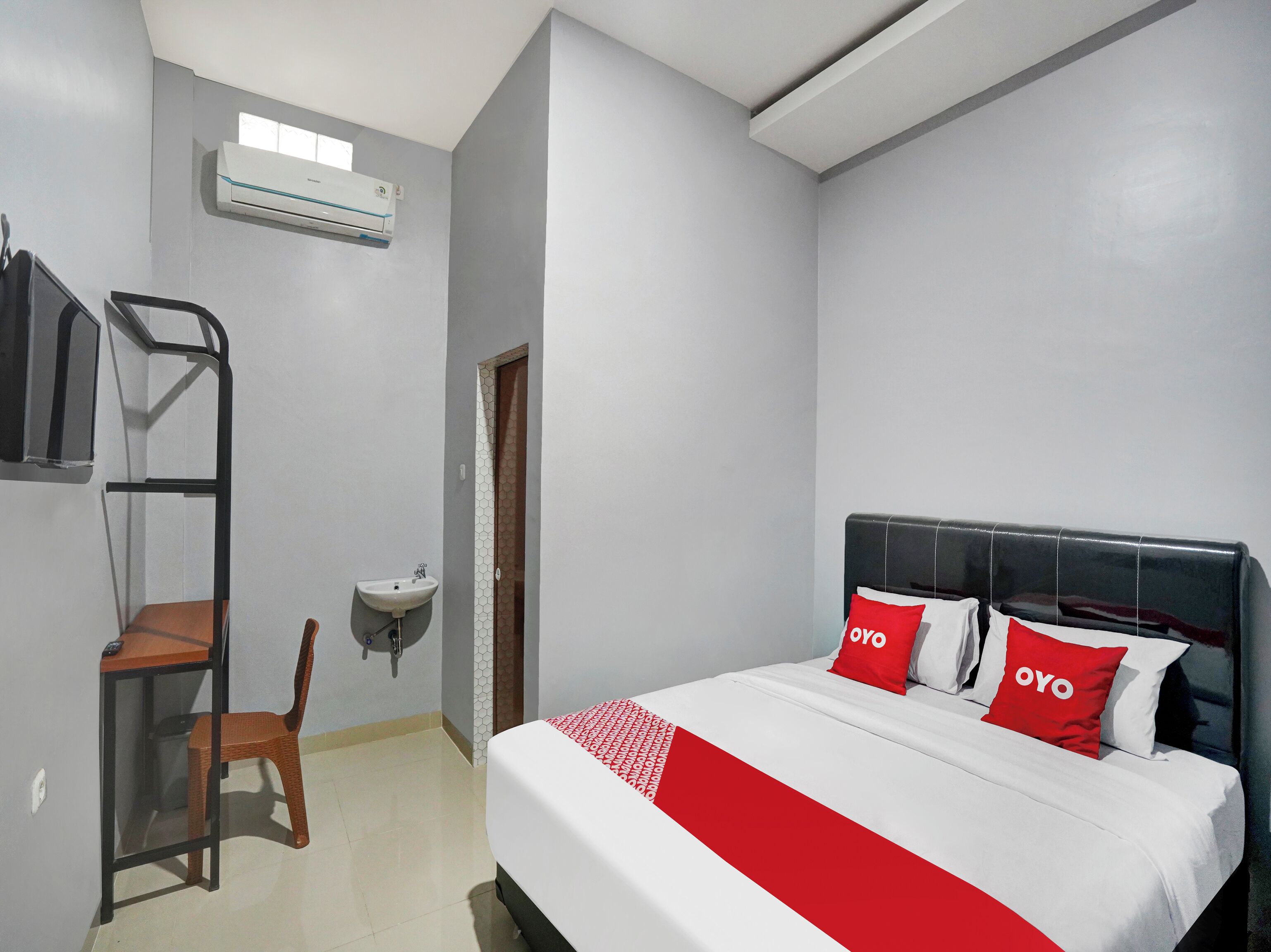 A hotel room with a bed, a desk, a chair, a sink, and an air conditioning unit.