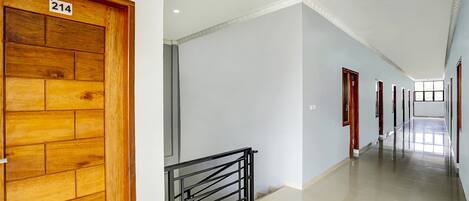 Un pasillo con una puerta de madera con la etiqueta 214, una barandilla de metal negro y un largo corredor con puertas a ambos lados.