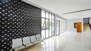 A spacious, modern waiting area with a row of metal chairs, large windows, and a staircase in the background. - Hotel O Beda Arga Near Rs Royal Prima Ayahanda (Medan)