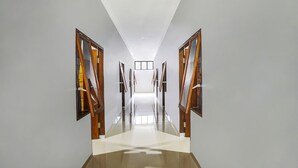 A modern hotel hallway with a polished floor, wooden doors, and framed artwork on the walls. - Hotel O Beda Arga Near Rs Royal Prima Ayahanda (Medan)