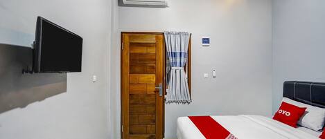 Una habitación de hotel con cama, televisor montado en la pared, puerta de madera y unidad de aire acondicionado.