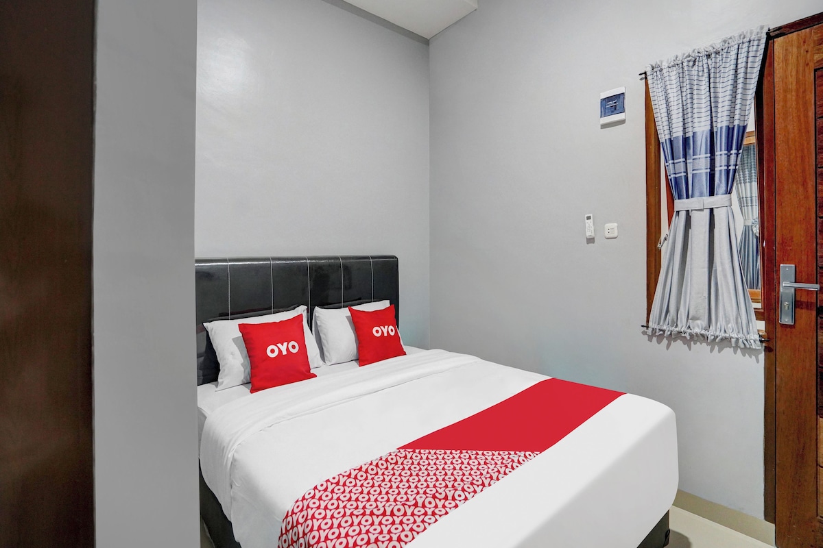 A bedroom with a bed, two pillows with 'OYO' text, a white and red bedspread, a window with curtains, and a door.