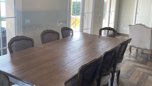 A dining area with a large wooden table, six upholstered chairs, and a hanging light fixture. - Villa dei Fenicotteri -Resort Marinagri 5 min from the beach! (Basilicata)