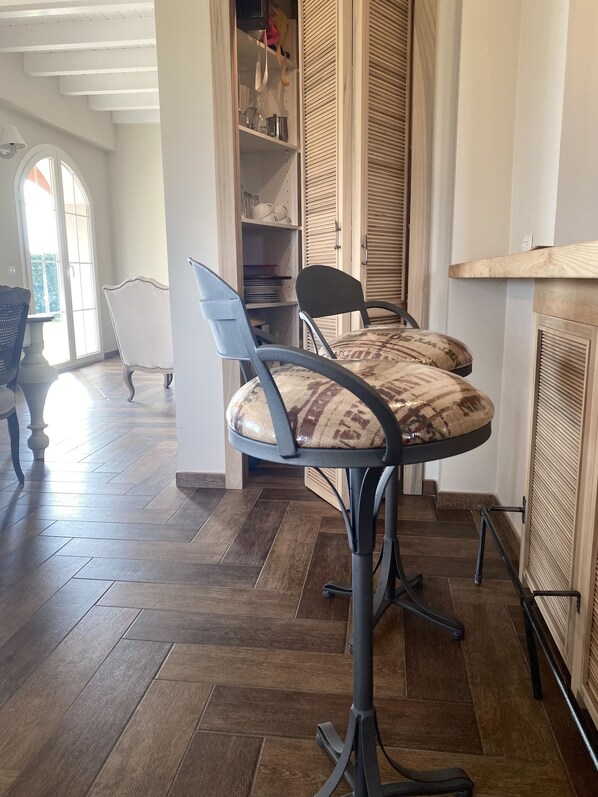 A dining area with a bar stool, a table, and a view of the outdoors through a window.
