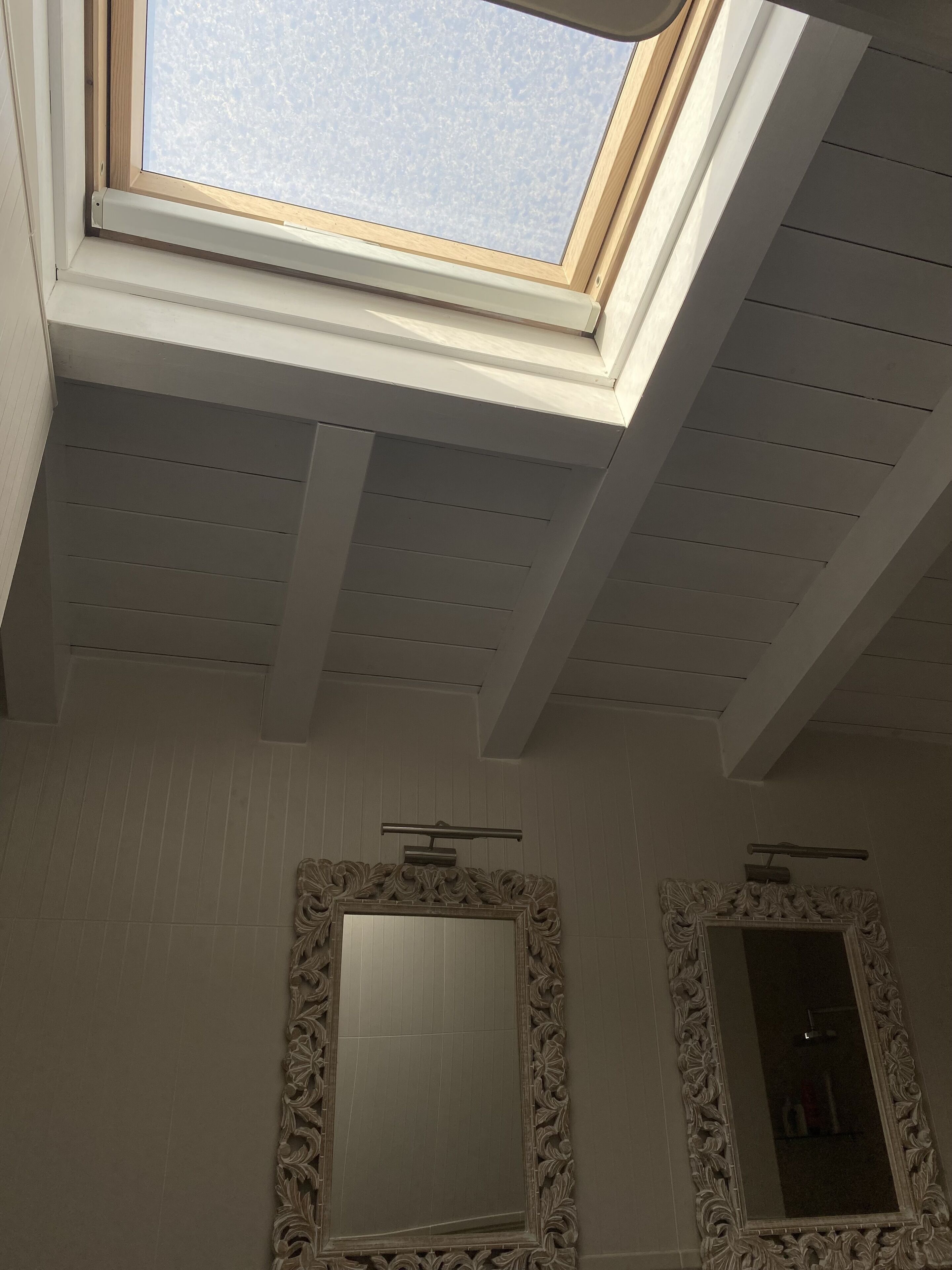 A skylight in a bathroom with two ornate mirrors.