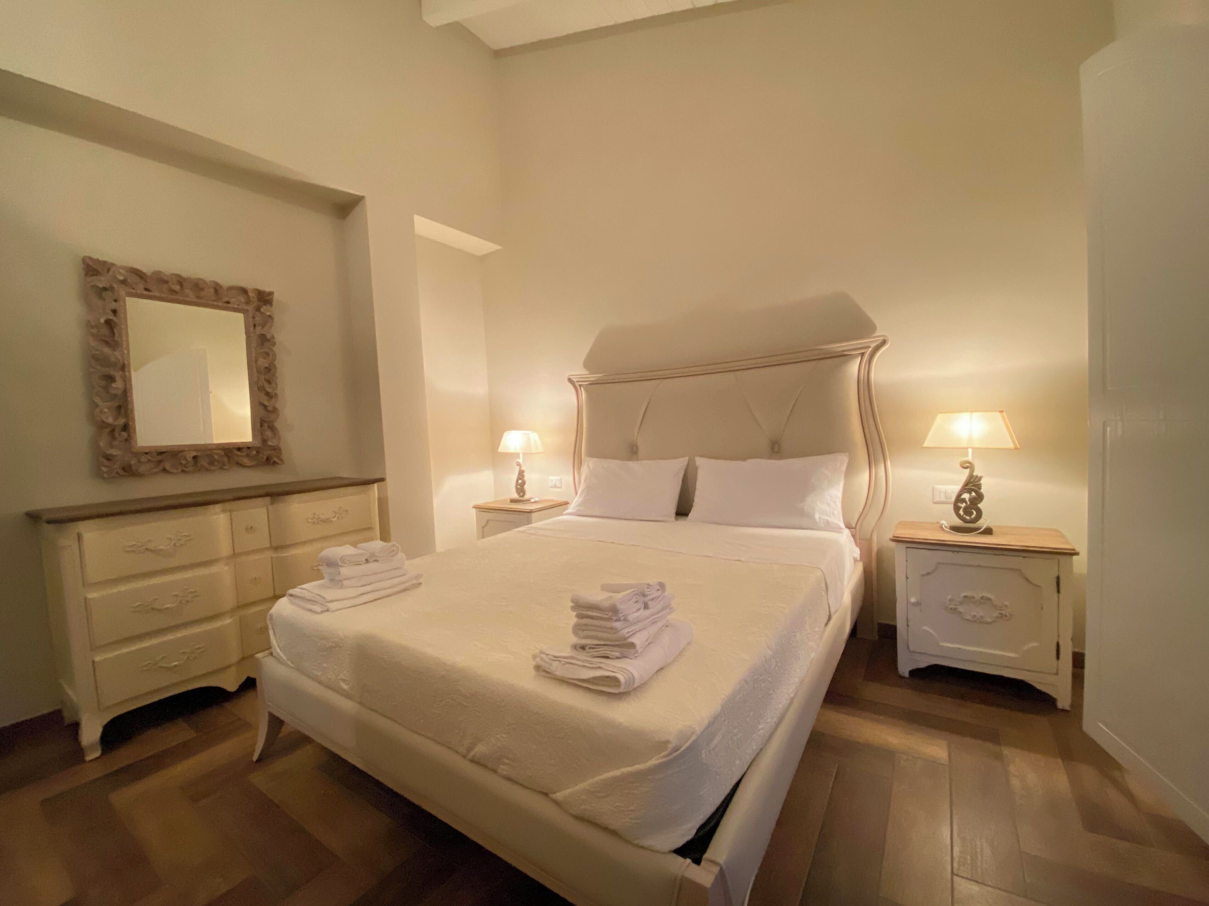 Um quarto bem arrumado com uma cama grande, duas mesas de cabeceira com luminárias, um penteoude e um espelho na parede.