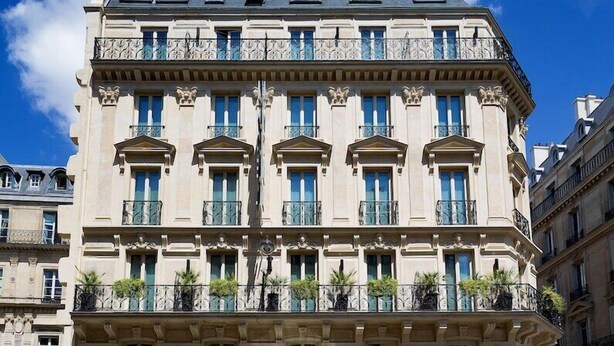 A multi-story building with a classic architectural style, featuring a central entrance with a black awning, multiple balconies with wrought iron railings, and a row of windows with blue shutters. - Hotel Chateaudun Opera (Paris)